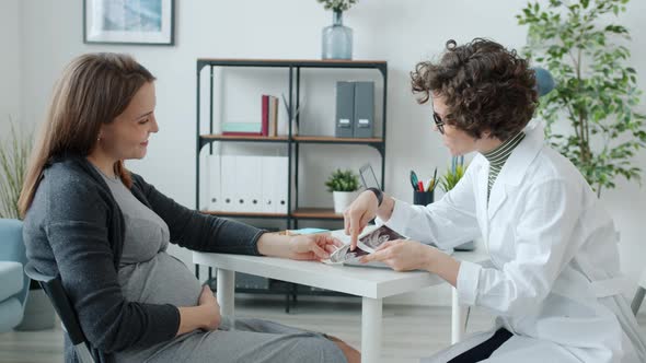 Female Gynecologist Talking To Pregnant Patient Discussing Ultrasound Image in Clinic
