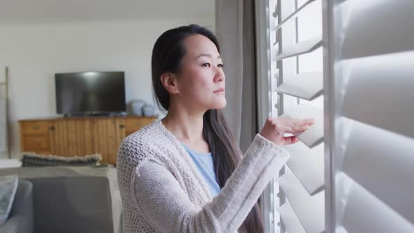 Profile of thoughtful asian woman standing at window, looking outside