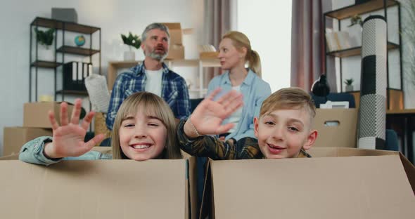 Boy and Girl Sitting in Carton Boxes and Waving Hands into camera