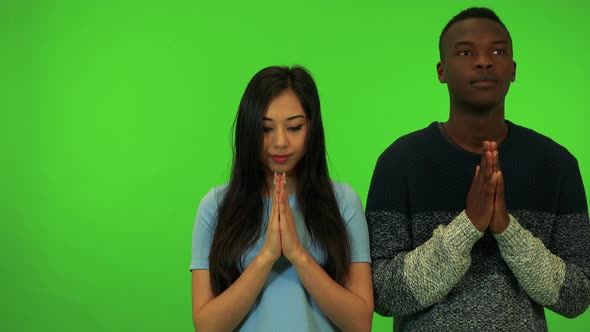 A Young Asian Woman and a Young Black Man Pray with Hands Clasped Together - Green Screen Studio