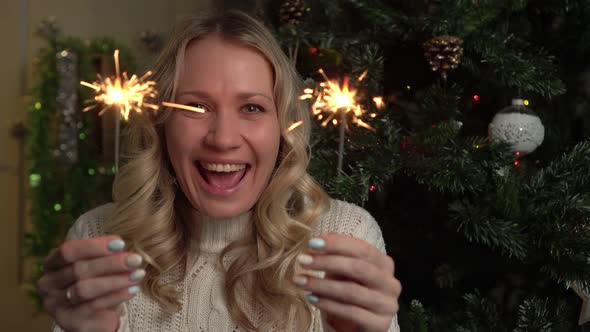 An Attractive Woman Holds a Burning Sparklers on a Christmas Tree