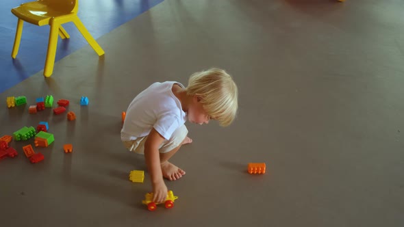 a Small Child Plays with a Construction Set and a Toy Car on the Floor