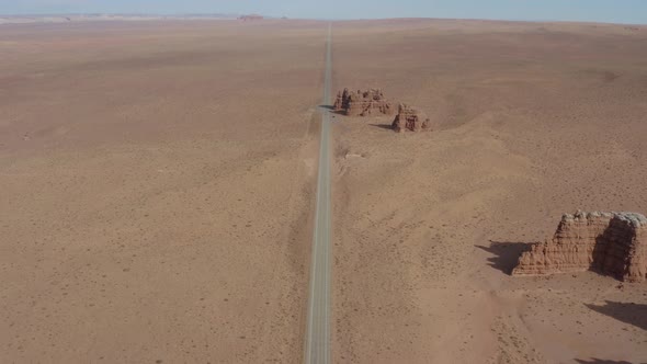Aerial view going over a desert road toward a small rock group formation off the side of a Utah high