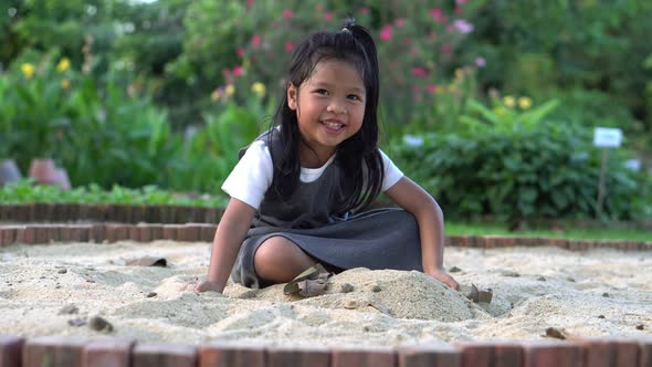 Little Asia girl sitting in the sandbox and playing whit toy shovel bucket
