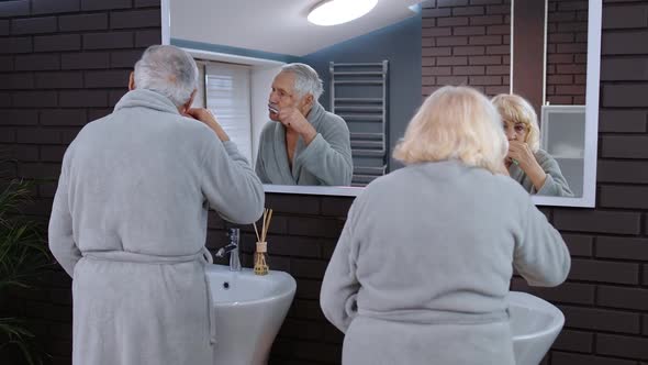 Senior Couple Man and Woman Brushing Teeth and Looking Into a Mirror at Luxury Bathroom at Home