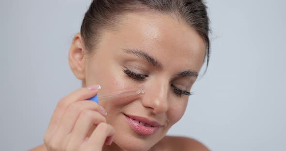 Close Up Portrait of Young Woman Applying Serum on Her Cheek Skin Care Gray Studio Background