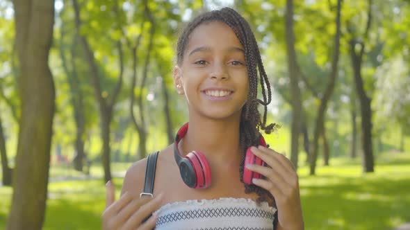 Close-up Portrait of Charming Happy Girl with Afro Pigtails and Brown Eyes Taking Off Headphones and