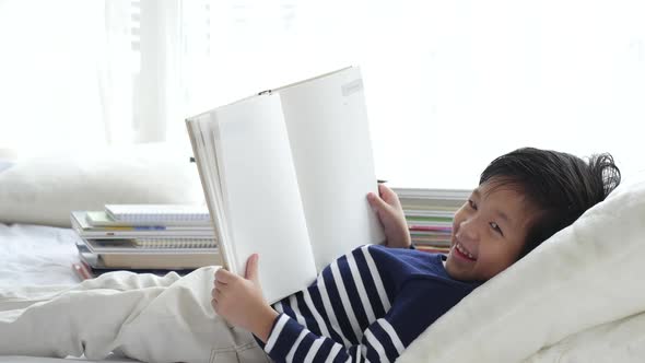 Cute Asian Child Reading A Book On White Bed