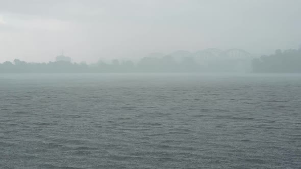 Wide Shot of Rain Falling on River with Misty City at the Background. Thunderstorm, Power of Nature