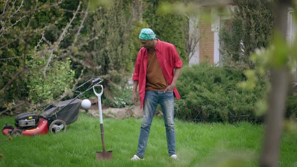 Confident Young Man Putting Shovel in Ground in Garden and Leaving