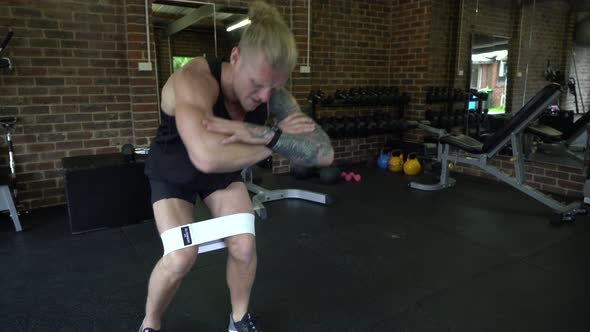 Tattooed man in home gym squat walk with resistance bands and finish