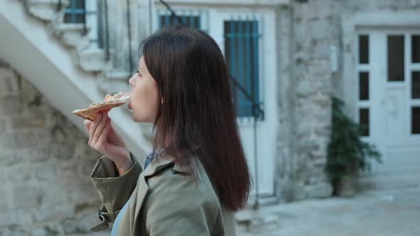 Slow motion Pretty young women in green coat walking and eating pizza in old town in spring time