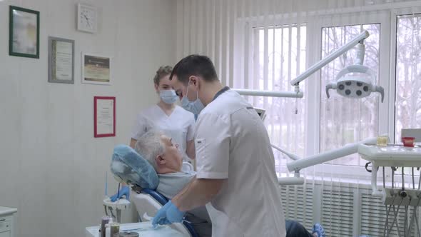 Dentist with Nurse in Protective Masks Preparing to Examine a Patient in Dental Clinic