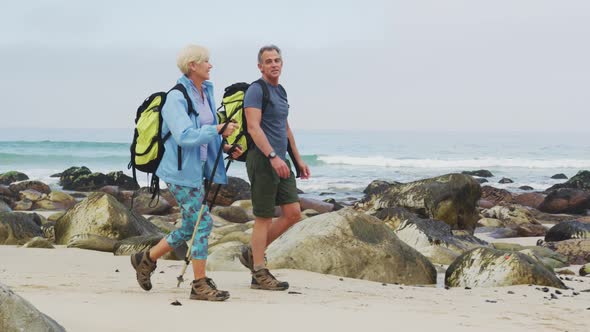 Senior hiker couple with backpack and hiking poles talking to each other and walking while hiking