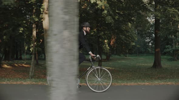 Businessman Riding a Bike in City Park Wearing Helmet and a Bag Side View