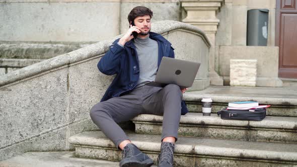 Man using laptop while speaking on mobile phone sitting on stone staircase