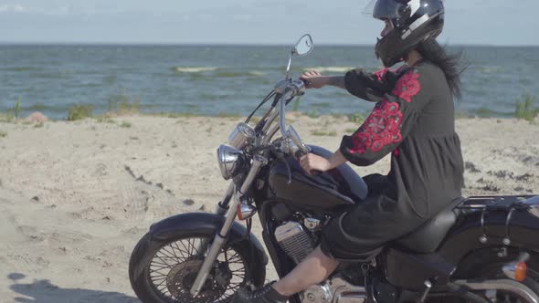 The Girl Wearing Black Helmet Sitting on the Motorcycle Looking Away on the Beach of the Sea