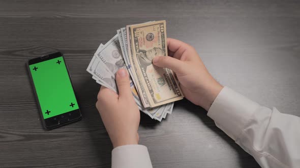 Businessman Counting Money and Green Screen Phone Laying Nearby on the Table