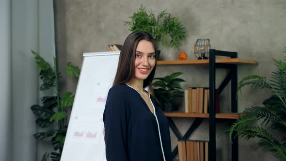 Smiling woman business coach turns head looking camera on background whiteboard