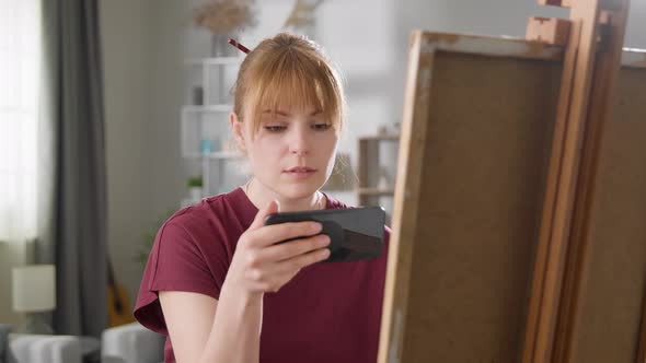 Young Attractive Woman Learns to Draw Using Video Lesson on Mobile Phone