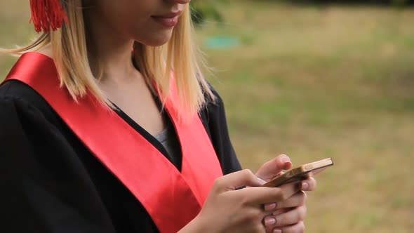 Beautiful Blond Graduate Texting on Smartphone After Graduation Ceremony