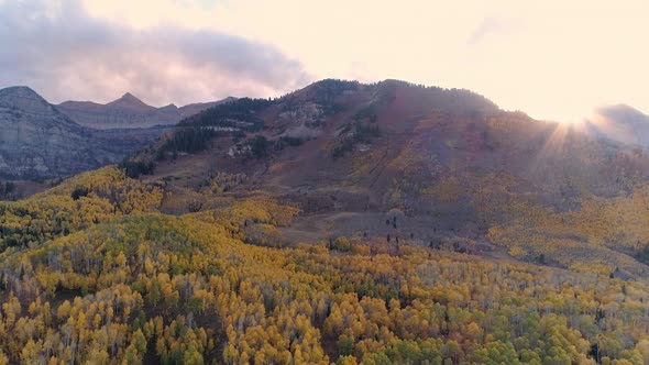 Sun peaking over mountain range covered in colorful foliage