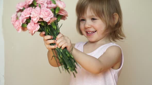 Little Girl Holds Bouquet of Flowers Pink Carnations Looks at Camera Smiles and Smells Flowers