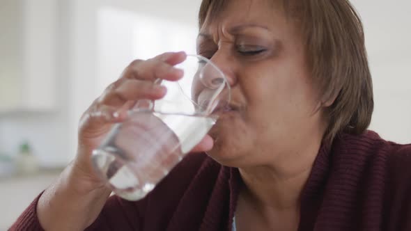 Sad, sick african american senior woman drinking water after taking medication