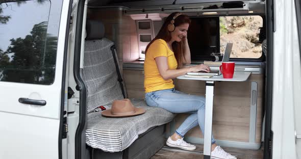 Senior caucasian woman using laptop and wireless headphone inside mini van camper