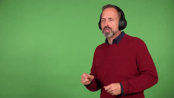 A Middleaged Handsome Caucasian Man Dances to Music with Headphones on and a Smile  Green Screen