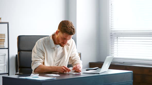 Professional accountant with beard sorts small paper receipts on grey table