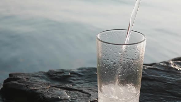 Soda Water is Poured Into a Steamedup Tall Glass Standing on a Rocky Seashore