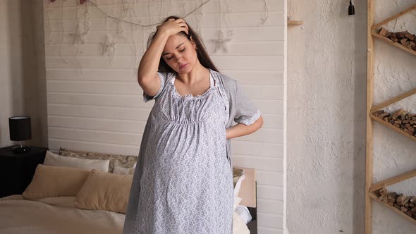 Portrait of a Pregnant Woman in Home Pajamas and a Bathrobe with Back Pain