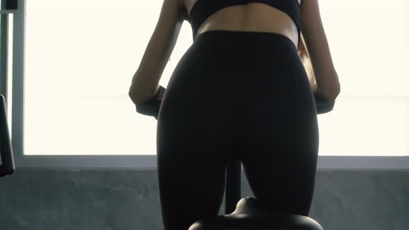 Rear View of Sporty Woman Riding Stationary Bike at the Gym