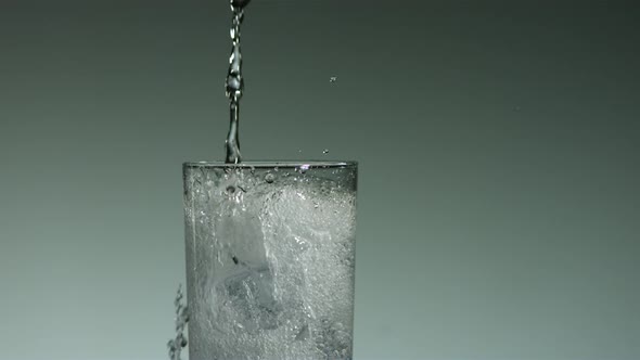 Carbonated liquid pouring into glass filled with ice 