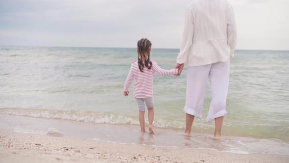 Mother With Little Daughter Walking Along the Sea Happy Family on the Beach Mother Holds Hand Little