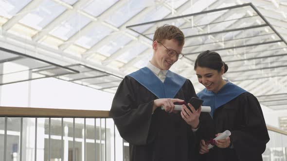 Two Young Graduates Using Smartphone