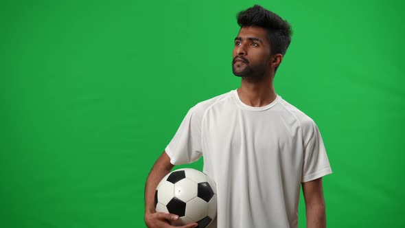 Concentrated Middle Eastern Young Man with Soccer Ball Looking Away Standing on Green Screen