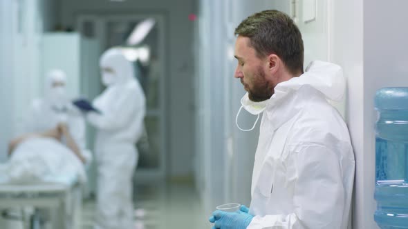 ER Doctor in Protective Suit Drinking Water on Break in Hospital