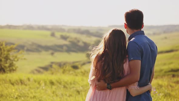 Young Couple Standing in the Nature on Sunset, Looking Somewhere in the Distance Pointing To It