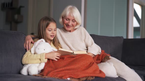 Happy girl with her grandmother reading book on the sofa
