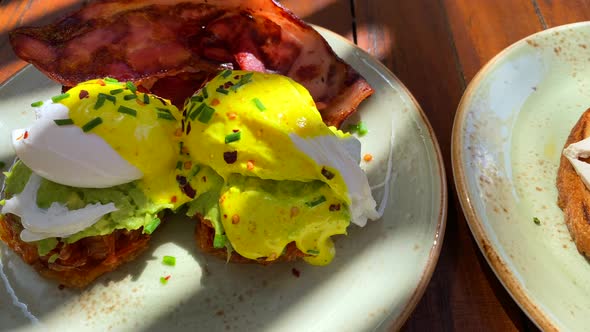 Delicious Eggs Benedict breakfast dish with crispy bacon, hollandaise sauce and avocado on sweet pot