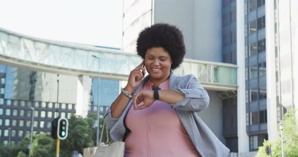 Happy plus size biracial woman checking smartwatch and walking in city