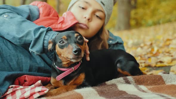 Girl Relaxes in the Autumn Forest with Her Miniature Pinscher