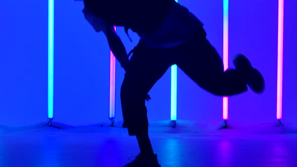 The Guy Is Dancing Breakdance in the Studio Against the Background of Multicolored Neon Lamps