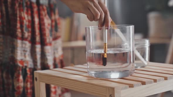 Female Painter Rinsing Brush in Glass of Water