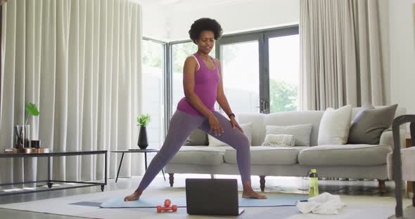 Happy african american wearing sportswear, exercising, using laptop