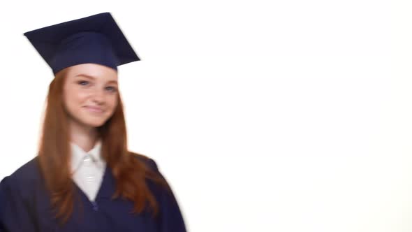 Smiling Ginger Young Graduate Girl in Blue Robe and Square Academical Cap Entering Frame Holding Her