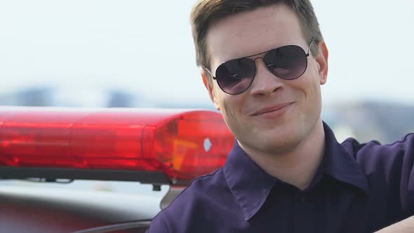 Patrol Officer in Glasses Standing Near Police Car Looking to Camera and Smiling