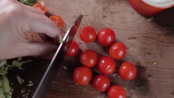 Top down view of woman cutting tomatoes on wooden chopping board. Medium shot